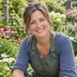 Vrouw met tuinschort glimlacht tussen bloeiende planten in een tuin
